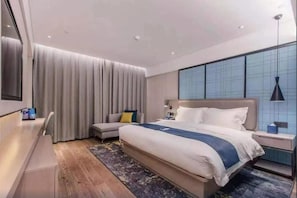 Habitació d'hotel moderna amb un llit gran, una taula de treball, una cadira i vista a la ciutat a través de grans finestres.