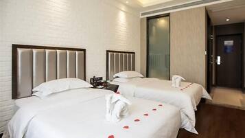 A hotel room with two beds, a wooden floor, and a white brick wall.