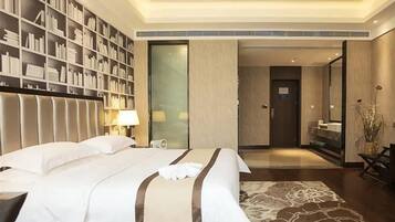 A hotel room with a large bed, a bookshelf, a desk, and a bathroom visible through an open door.