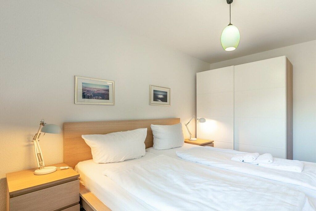 A hotel room with a bed, nightstands, a lamp, a wardrobe, and two framed pictures on the wall.