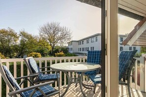 A balcony with a glass door, a round table, and blue-striped chairs. - 4 "Duckdalben" (ID 097) (St. Peter-Ording)