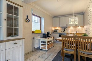 A compact kitchen with white cabinetry, a dining table with chairs, a coffee machine, and a hanging light fixture. - Holiday apartment 3 "Little Seagull" (ID 030) (St. Peter-Dorf)