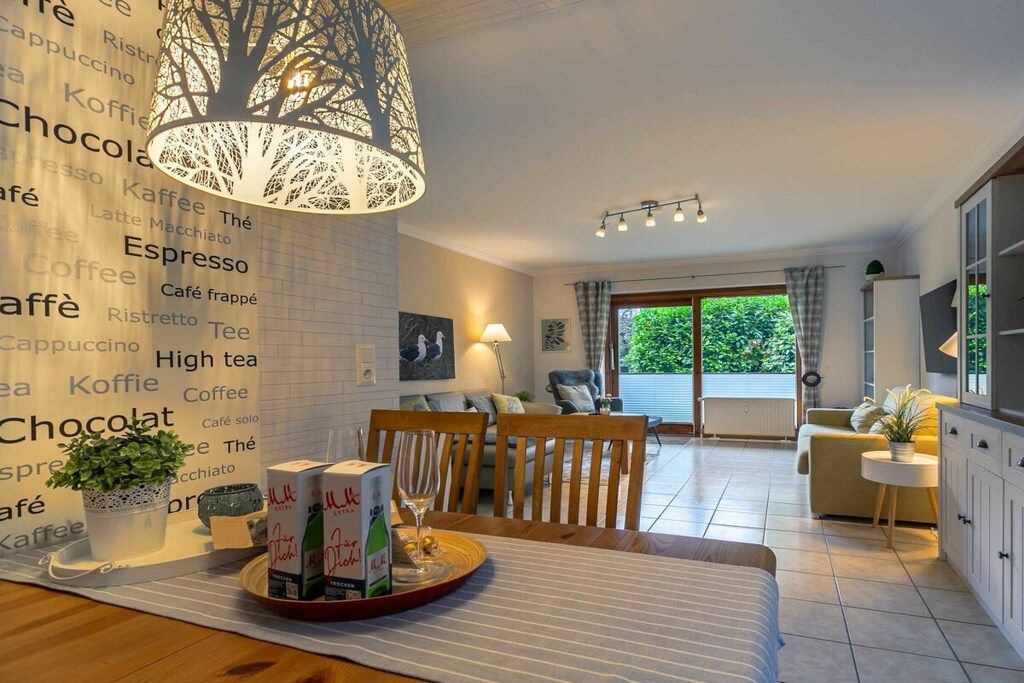 A modern living room with a dining area, a large tree-patterned light fixture, and a view of greenery outside.