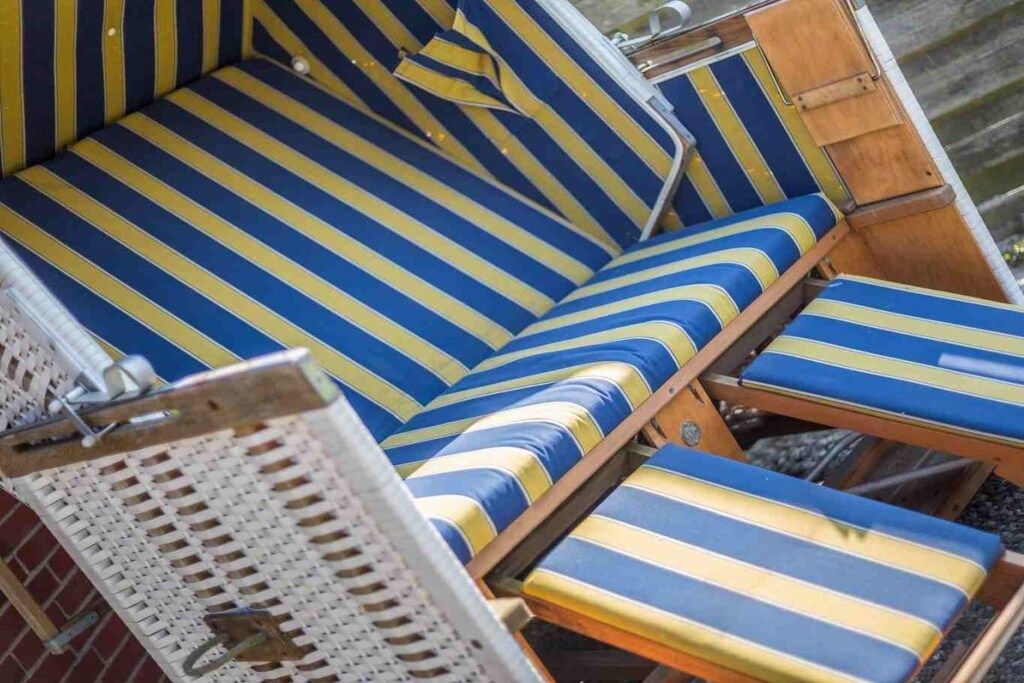 Une rangée de chaises longues à rayures et un banc doté d’un dossier en osier, qui font probablement partie d’un espace de détente aménagé près de la plage.