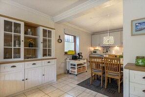 A kitchen with white cabinetry, a dining area with wooden chairs, and a small table with a kettle. - Holiday apartment 3 "Little Seagull" (ID 030) (St. Peter-Dorf)