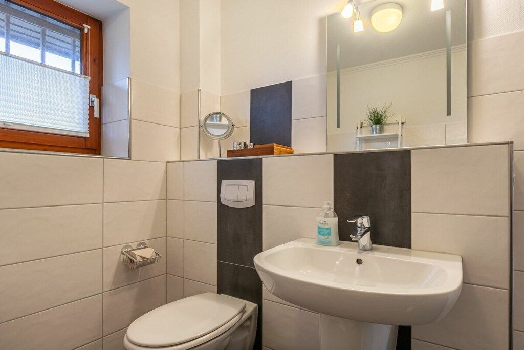 Ein Badezimmer mit Toilette, Waschbecken, Spiegel und einem Fenster mit Jalousien.