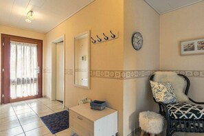 A room with a door, a mirror, a clock, a chair with a patterned cushion, and a small stool. - Holiday apartment 3 "Little Seagull" (ID 030) (St. Peter-Dorf)