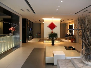 A modern lobby with a reception desk, a central plant, seating area, and a decorative red hanging ornament. - Jinjiang Inn (Tianjin)