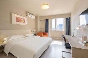 A hotel room with a large bed, a desk, a chair, a window with a city view, and a ceiling light. - Jinjiang Inn (Tianjin)