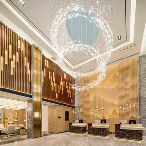 Un hall d’hôtel moderne comprenant un comptoir d’accueil, un espace salon et un luminaire circulaire original.