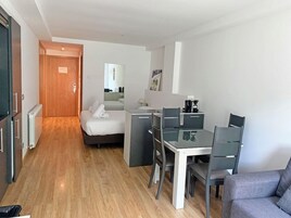Una habitación de hotel moderna con una cama, un escritorio con una silla, un sofá y suelo de madera.