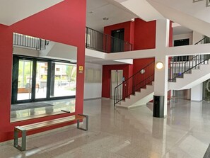 Un interior de varios niveles con una pared roja, una escalera y un banco.