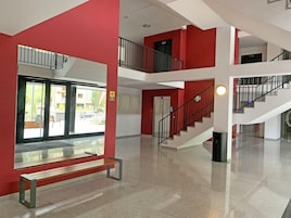 Un interior de varios niveles con una pared roja, una escalera y un banco.