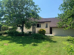 A single-story house with a tiled roof, surrounded by a well-maintained lawn and various shrubs.