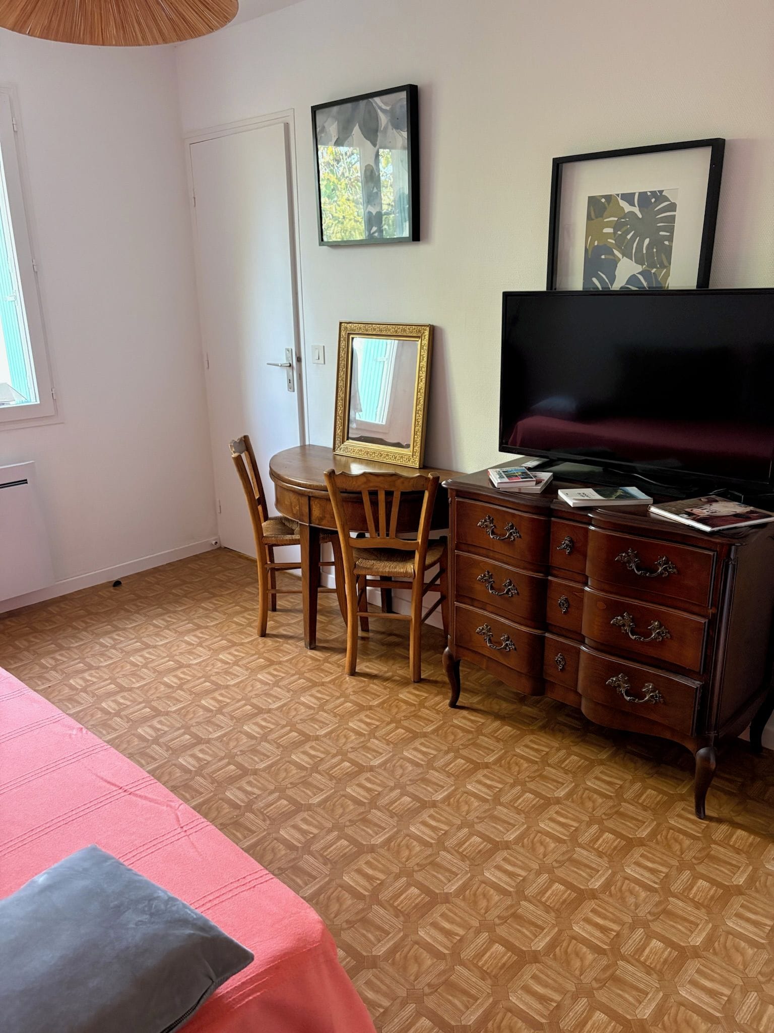 A room with a bed, a desk with a chair, a dresser, a television, and framed artwork on the wall.