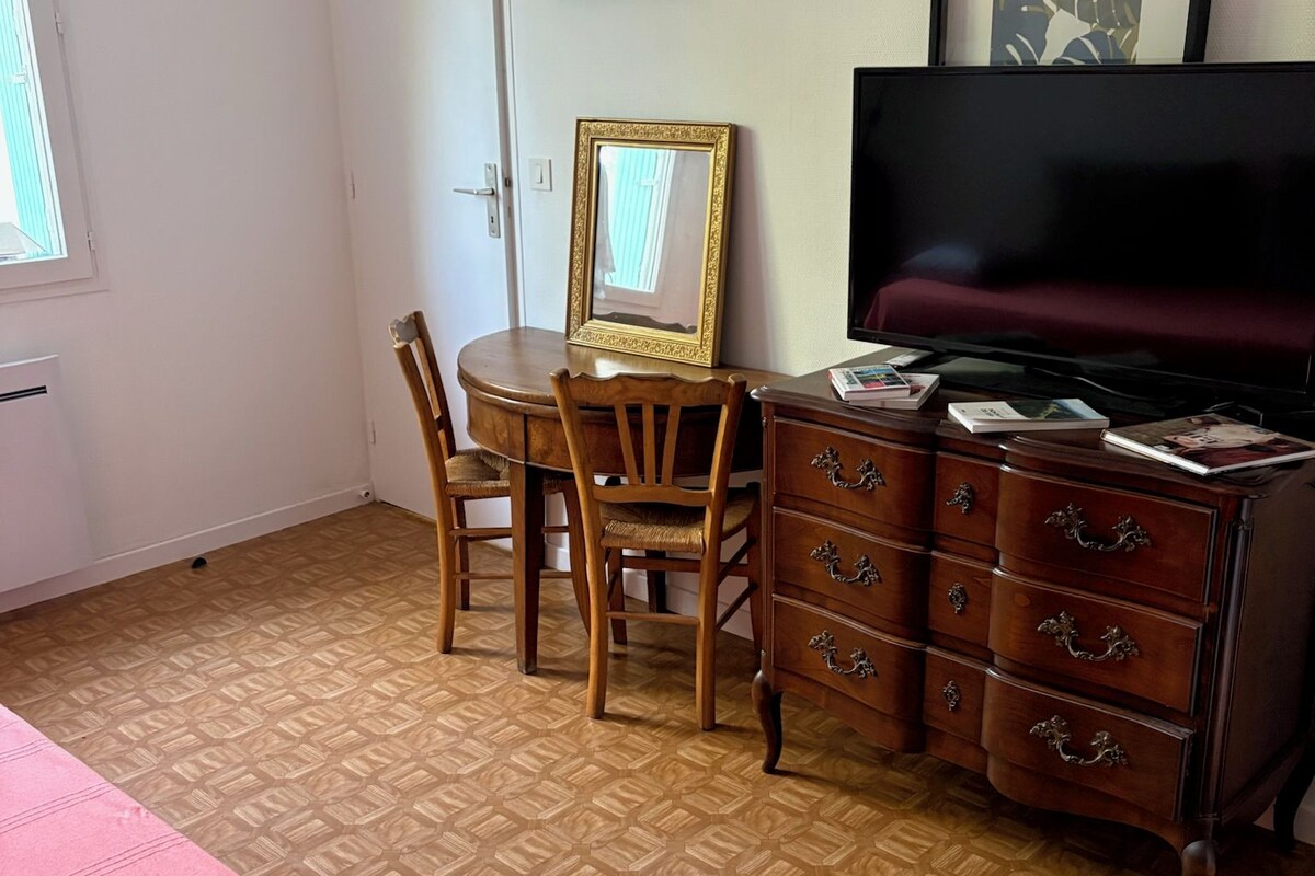 A room with a bed, a desk with a chair, a dresser, a television, and framed artwork on the wall.