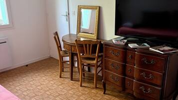 A room with a bed, a desk with a chair, a dresser, a television, and framed artwork on the wall.