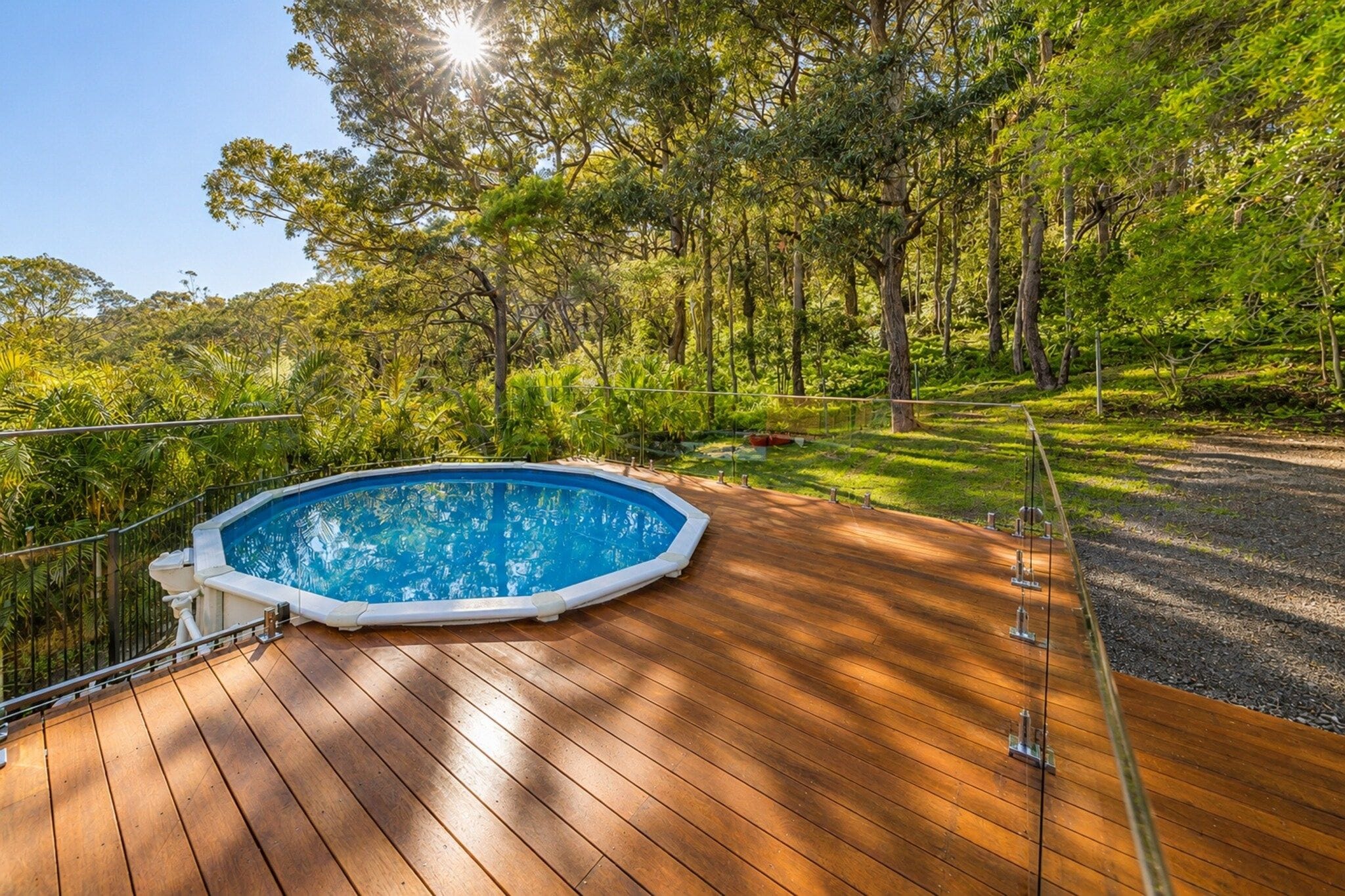 An outdoor swimming pool with a wooden deck, surrounded by lush greenery and trees.