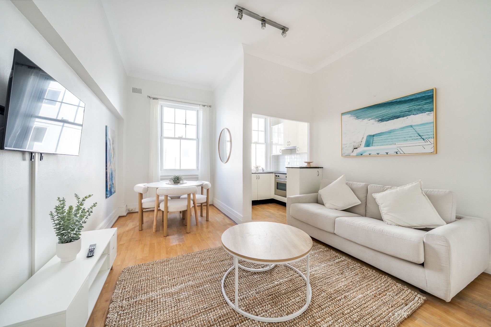 Un salon moderne avec un canapé blanc, une table basse ronde et un coin repas comprenant une table et des chaises blanches.