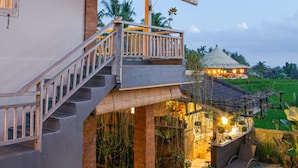 Un bâtiment à deux étages doté d’un balcon, d’un escalier et d’un espace extérieur bien éclairé, agrémenté de plantes et de mobilier.