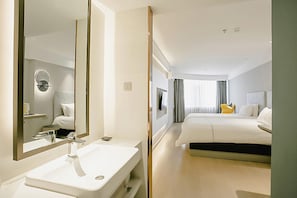 A modern hotel room with a large bed, a bedside table, a TV, and a bathroom with a sink and mirror. - Magnotel (Jinzhong)