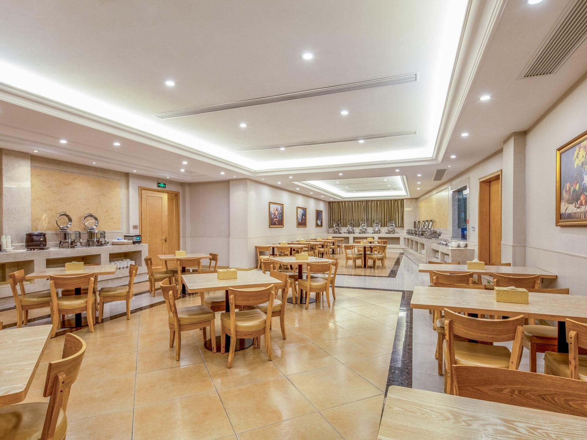 A spacious dining area with multiple tables and chairs, a counter with a coffee machine, and a painting on the wall.