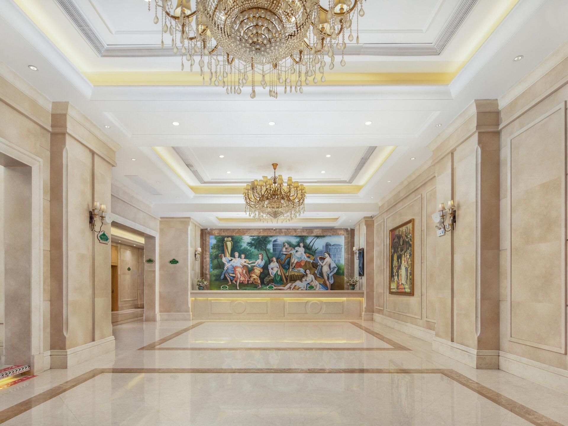 A spacious lobby with a large chandelier, marble flooring, and classical artwork on the walls.