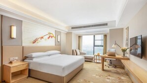 A hotel room with a large bed, a desk, a chair, a TV, and a window with a city view. - Vienna International Hotel (Xiangyang)