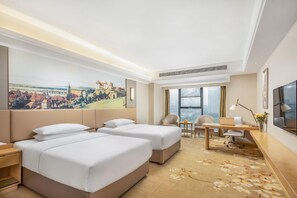 Une chambre d’hôtel avec deux lits, un bureau, une chaise, une télévision et une grande fenêtre donnant sur le paysage urbain.