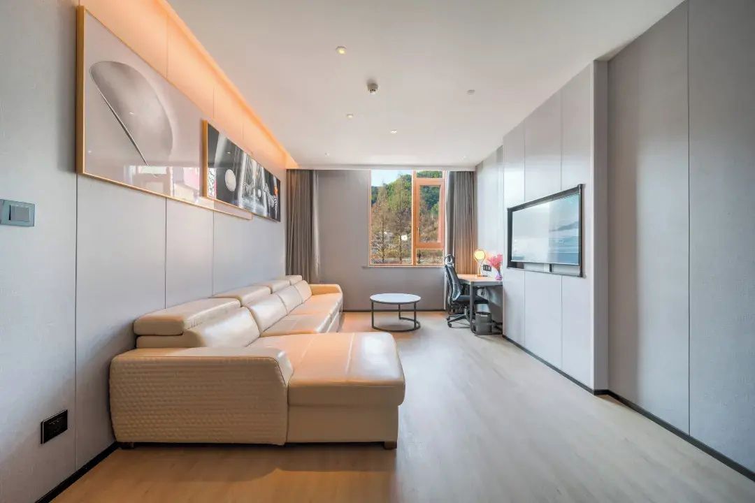 A modern living room with a sectional sofa, a dining area with a table and chairs, and a large window providing a view.