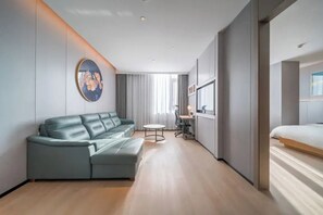 A modern hotel room with a sofa, a small round table, a bed, and a painting on the wall. - Microtel by Wyndham Huangshan Tangkou (Huangshan)
