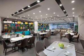 A modern restaurant with multiple dining tables and chairs, a bar area, and a wall displaying various food items. - Microtel by Wyndham Huangshan Tangkou (Huangshan)