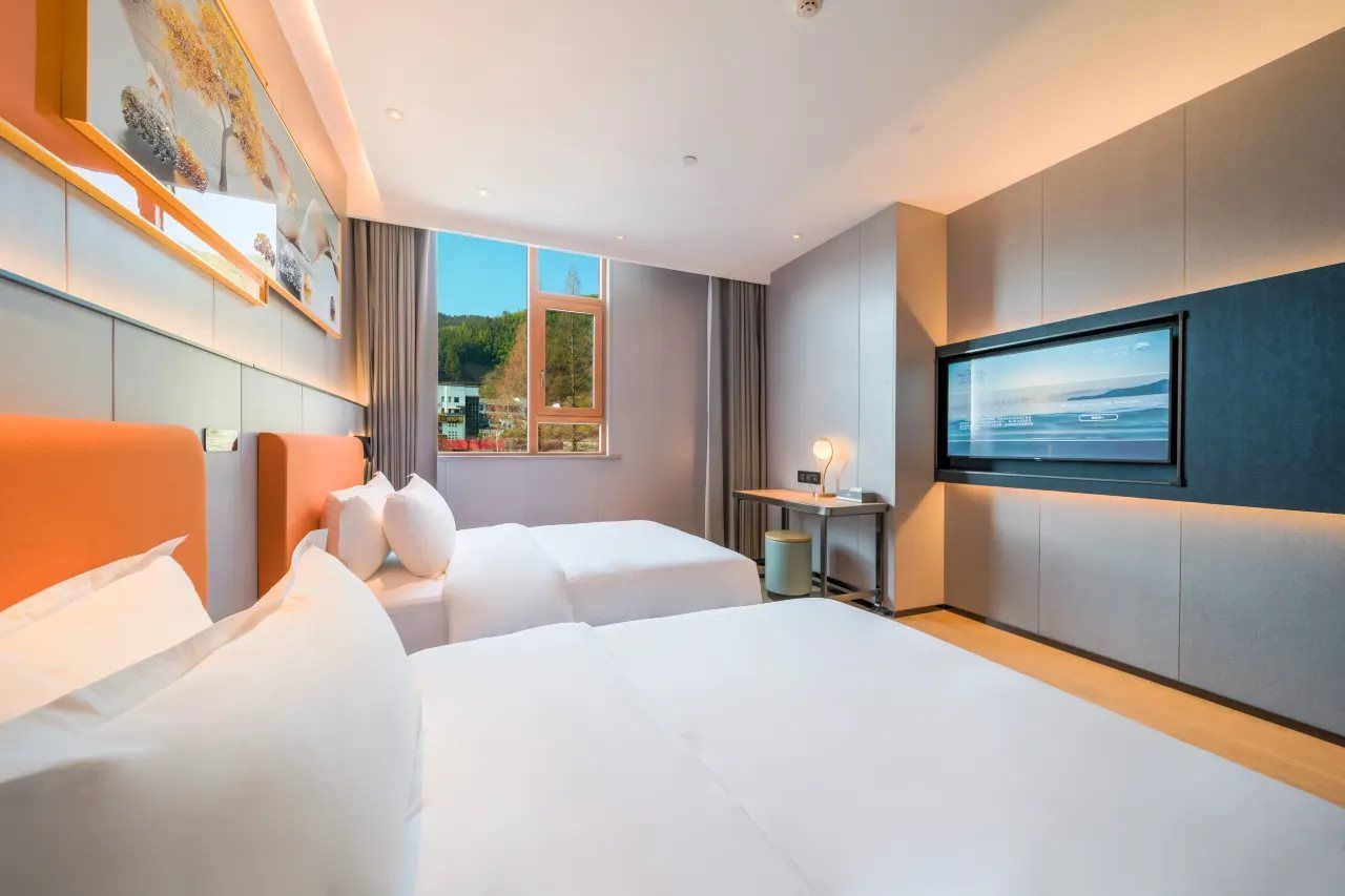 Quarto de hotel com duas camas, uma janela grande, televisão de tela plana e um quadro na parede.