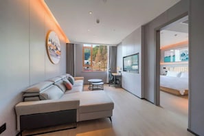 Una habitación de hotel moderna con sofá modular, una mesita redonda, televisión y cama.