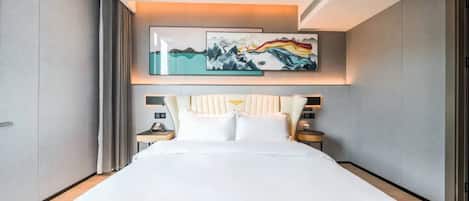 A modern hotel room with a large bed, a headboard with a decorative panel, a bedside table with a lamp, and a wall-mounted artwork above the bed.