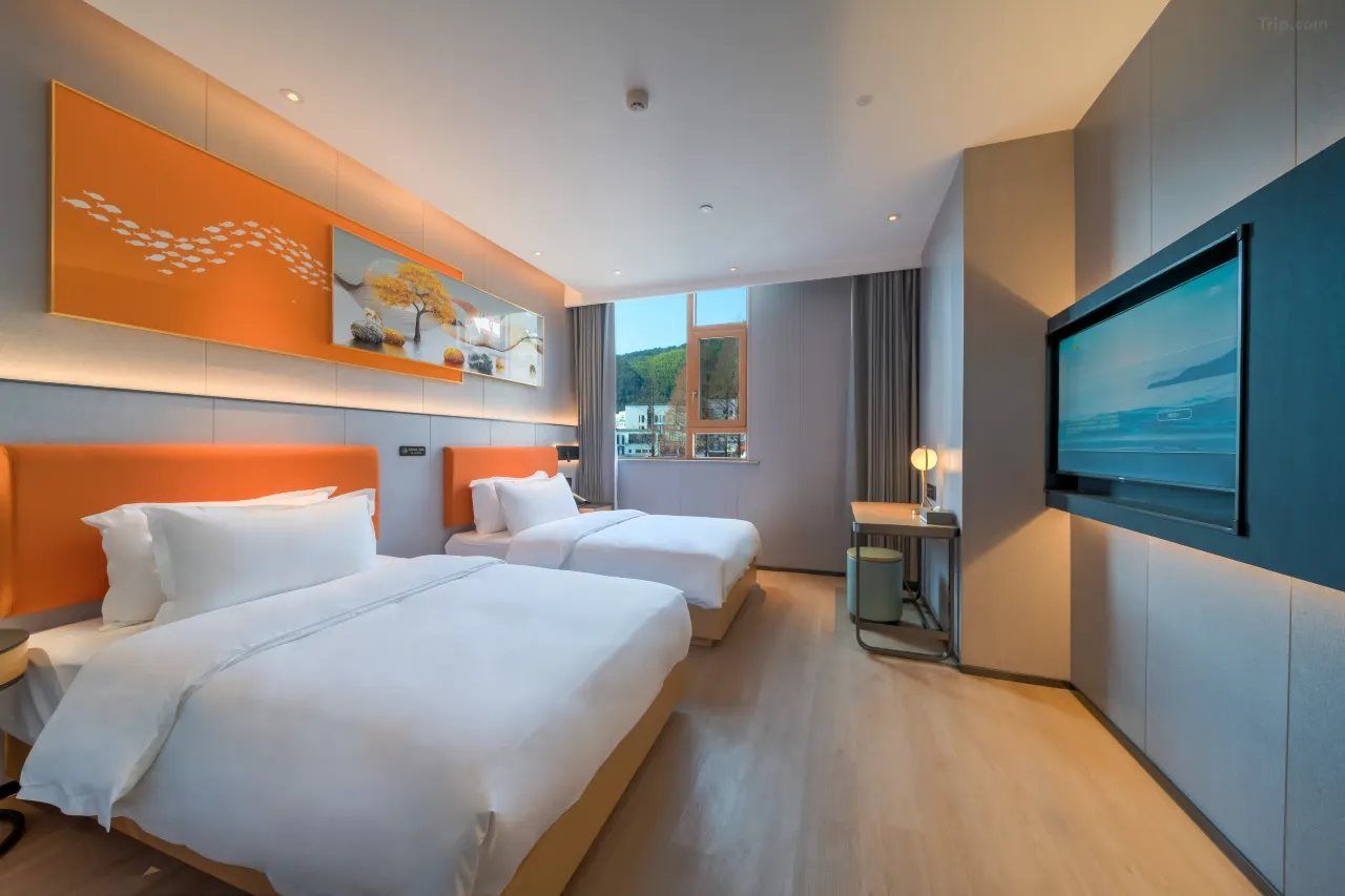 A hotel room with two beds, a television, and a window with a view of the outdoors.