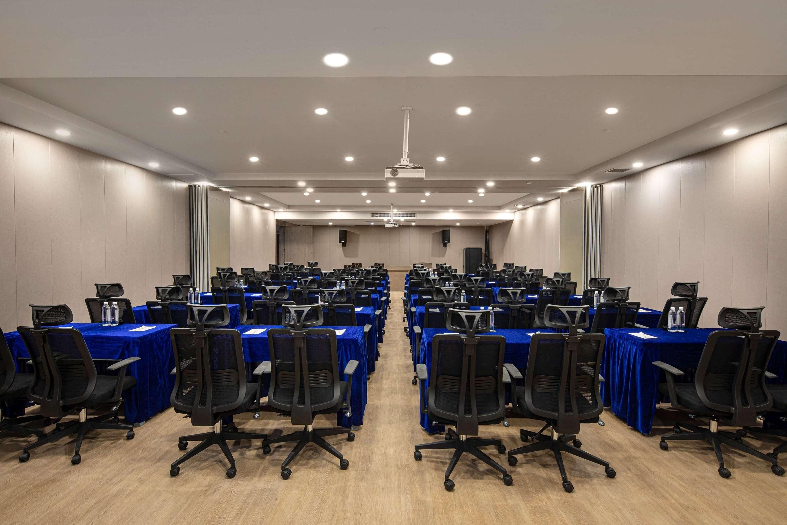 A conference room with rows of tables and chairs, equipped with projectors and speakers.