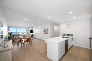 Una cocina moderna con una isla central, un comedor con vistas y un espacio de sala de estar con sofá y mesa.