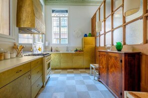Eine Küche mit Schachbrettboden, Holzschränken, einem Gasherd und einem Fenster mit Gitterstäben.