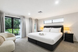 A modern bedroom with a large bed, a bedside table with a lamp, and a view of greenery outside. - Spacious 4-Bed Retreat Near Meadow Springs (Meadow Springs)