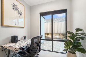 A room with a dining table, chairs, a speaker, a framed picture, and a large window with a view of a building and a plant. - Spacious 4-Bed Retreat Near Meadow Springs (Meadow Springs)