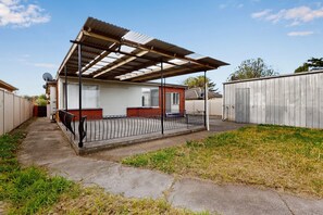 A covered outdoor area with a bench, a metal fence, and a building with a window.