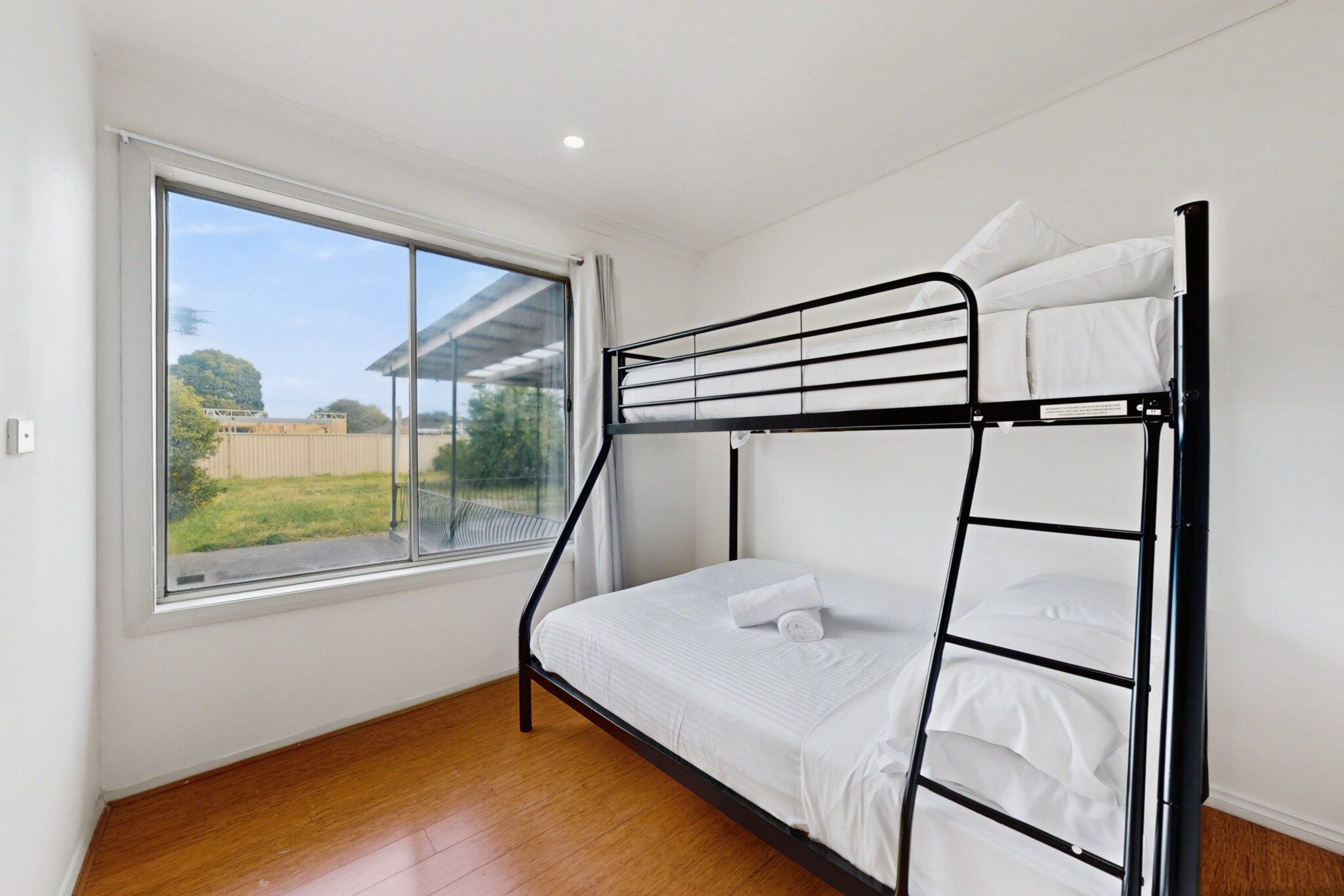A bunk bed with white bedding in a room with a large window and wooden flooring.