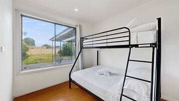 A bunk bed with white bedding in a room with a large window and wooden flooring.