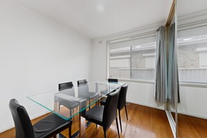 A modern room with a glass-top table and black chairs, large windows with curtains, and a wooden floor. - Spacious 4-Bed House with Garden in Glenroy (Glenroy)