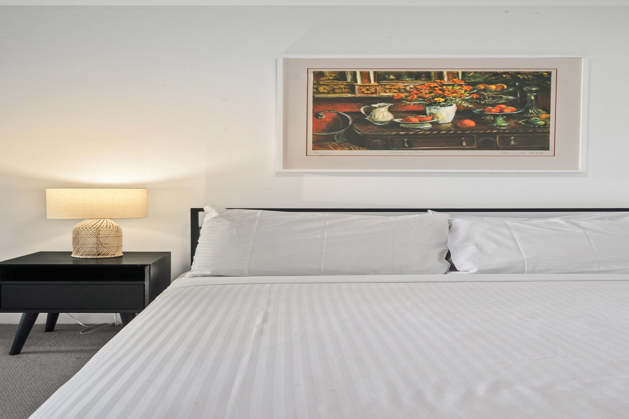 Une chambre d’hôtel avec un lit, une table de chevet avec une lampe et un tableau encadré au mur.