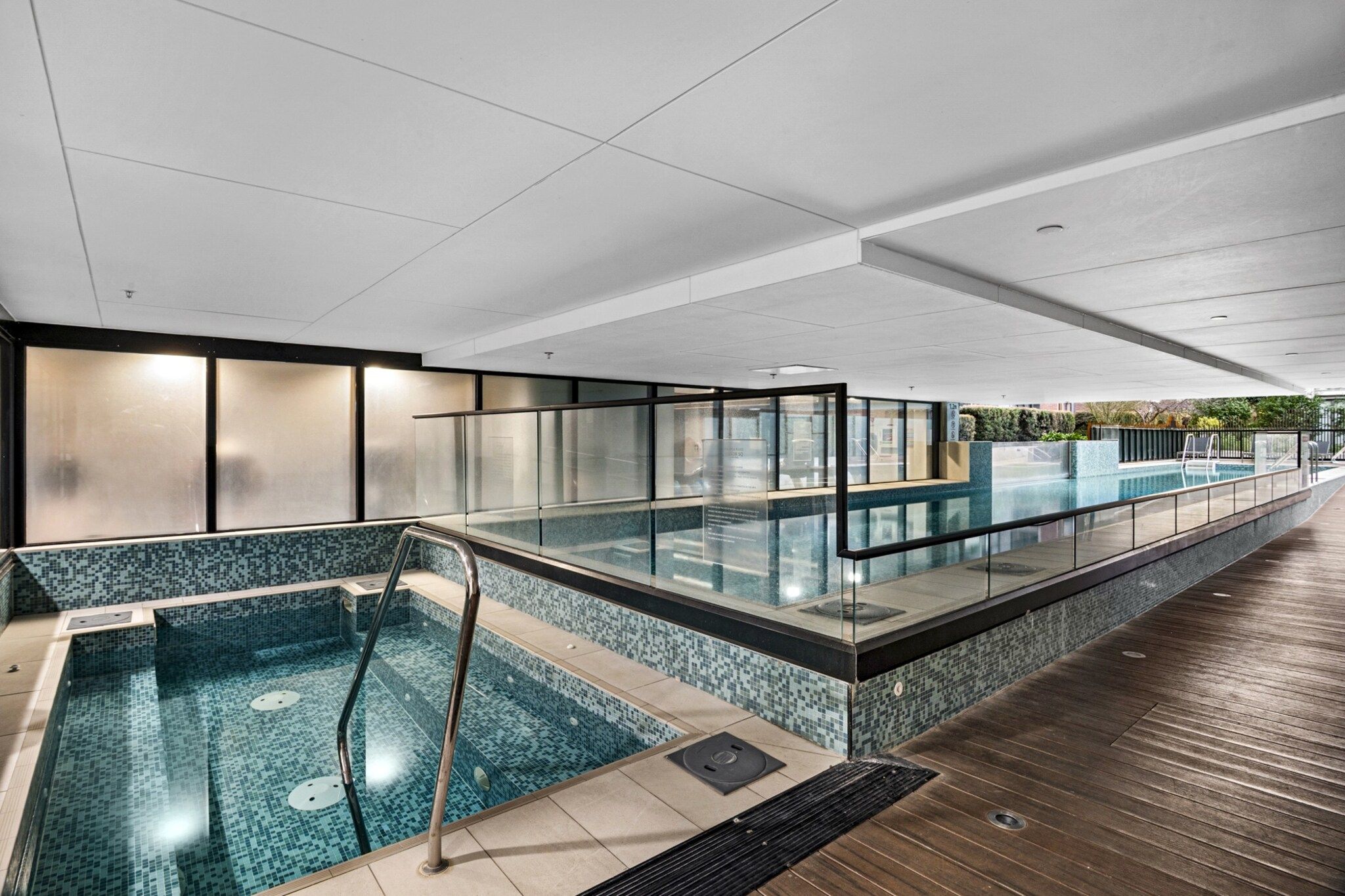 Una piscina interior moderna con barandillas de vidrio y una zona de terraza de madera.