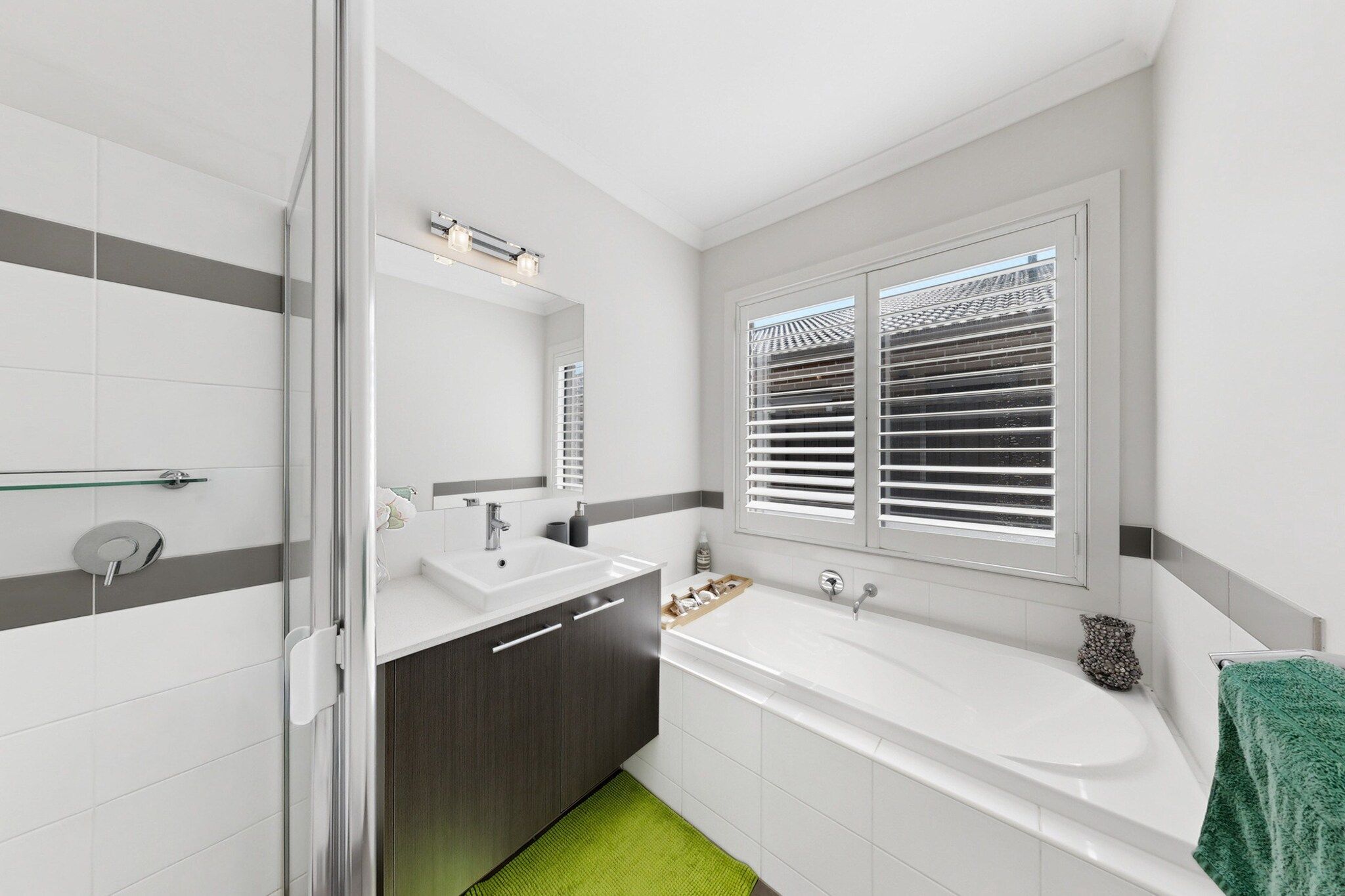 Ein modernes Badezimmer mit Dusche, zwei Waschbecken, einer großzügigen Badewanne und einem Fenster mit Jalousien.