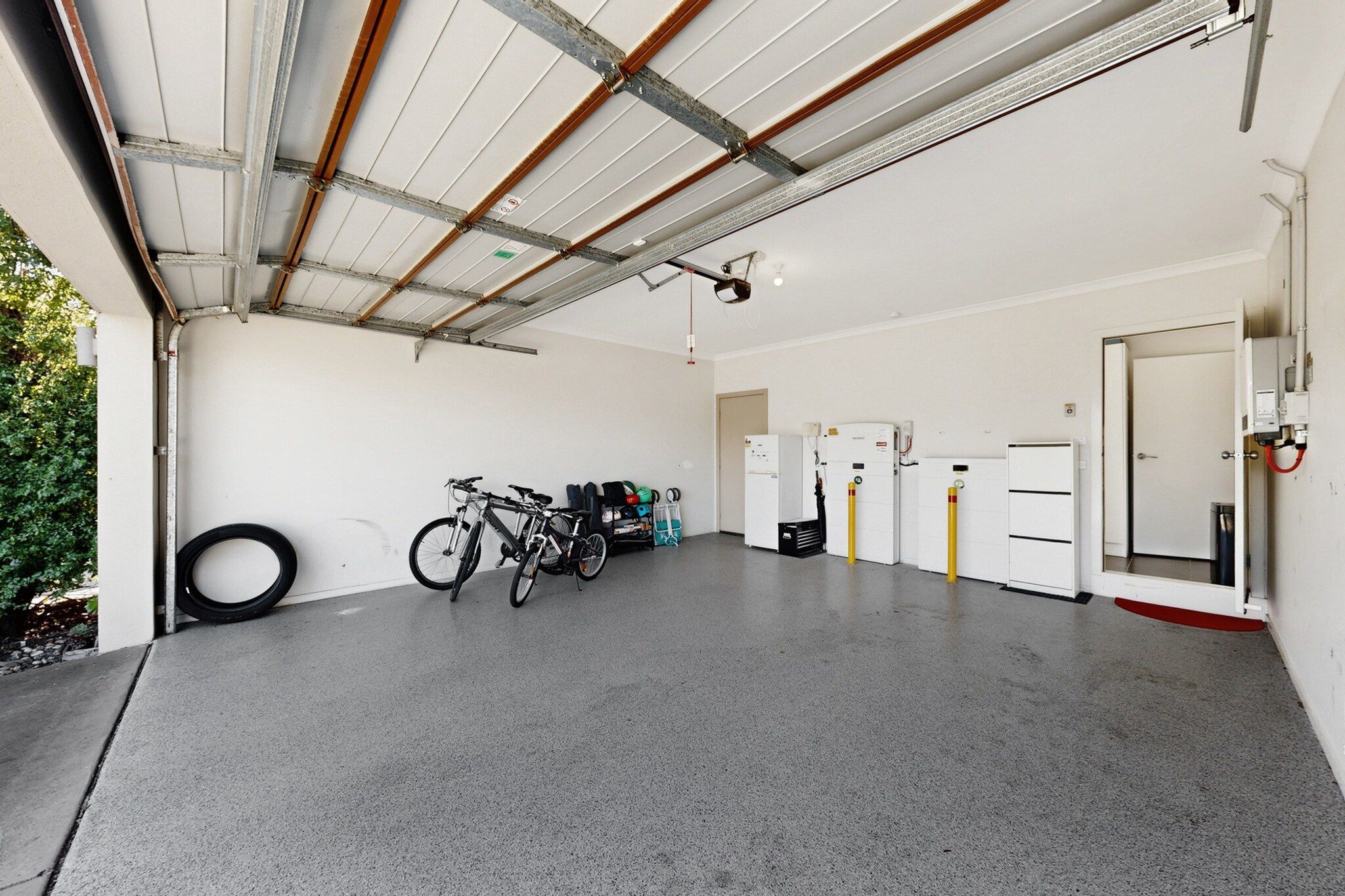 A garage with a concrete floor, bicycles, a tire, and electrical panels.