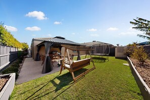 A backyard with a wooden swing set, a barbecue area, and a trampoline. - Family 3-Bed Retreat in Point Cook (Point Cook)
